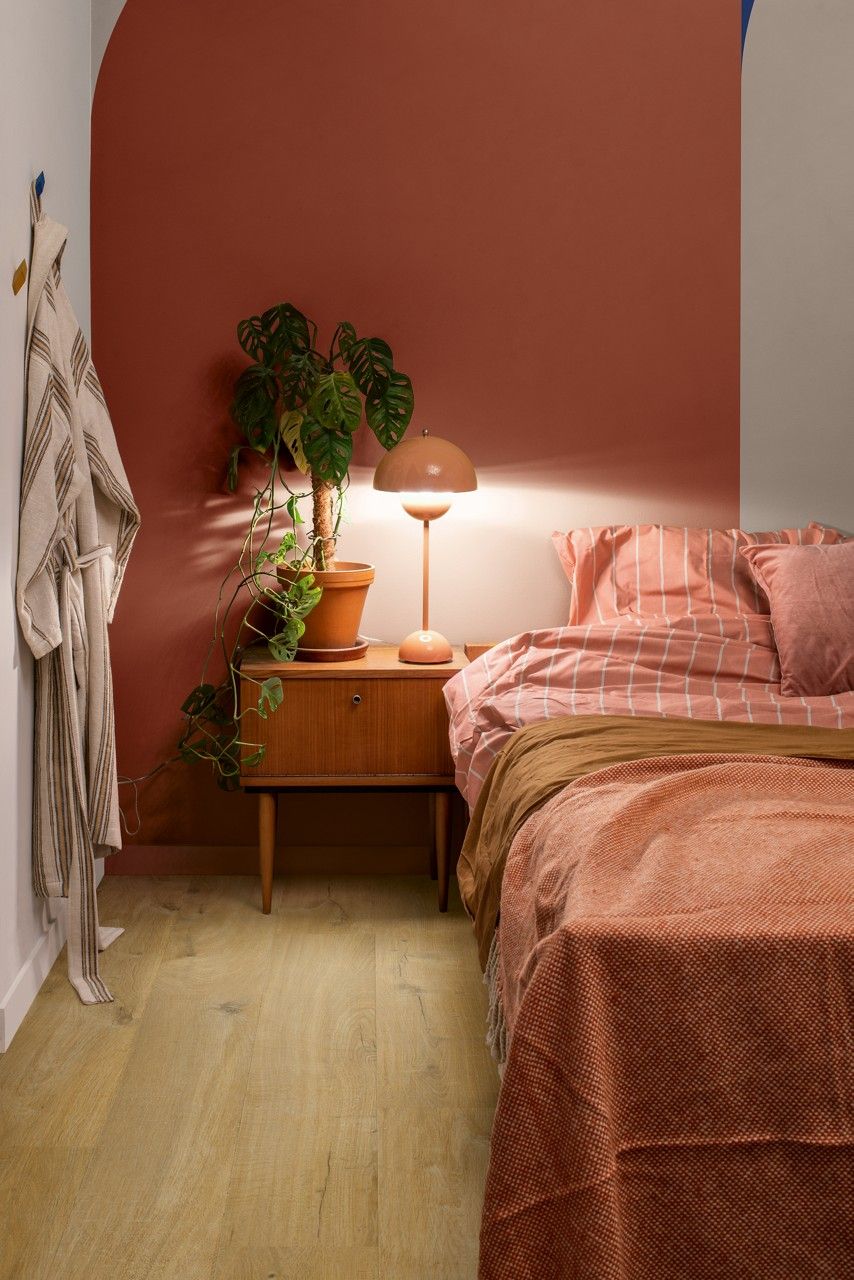 Bedroom with terracotta accent wall, wooden nightstand, bed with red patterned bedding, and floor lamp.