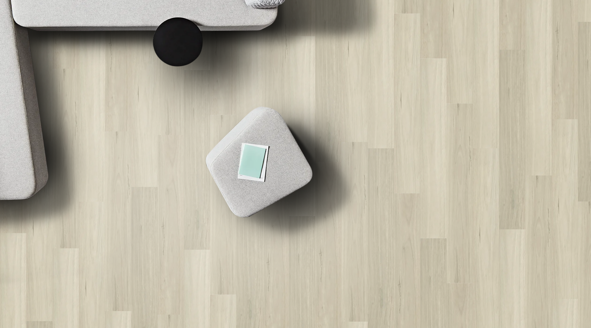 Overhead view of a living room scene with a white couch, small stool, and wooden floor. A card rests on the stool.