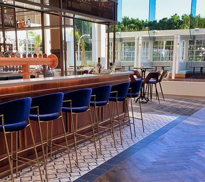 A Row of Blue Bar Stools Are Lined up In Front of A Bar in A Restaurant — Tony Di Milia Flooring in Unanderra, NSW