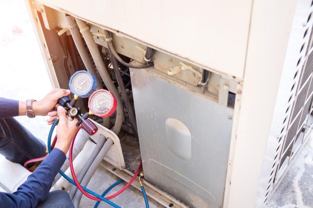 Technician connecting gauges to an outdoor air conditioner unit for maintenance