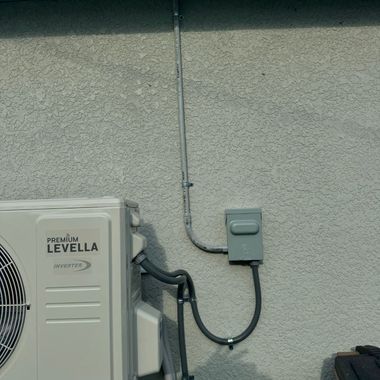 Outdoor wall-mounted air conditioner unit with conduit and electrical box on a beige stucco wall