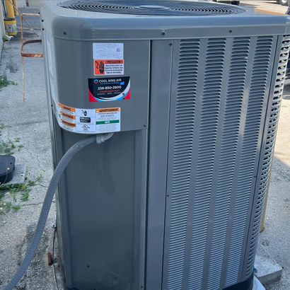 Gray outdoor air conditioner unit with vented side panels and service labels on a concrete pad outdoors