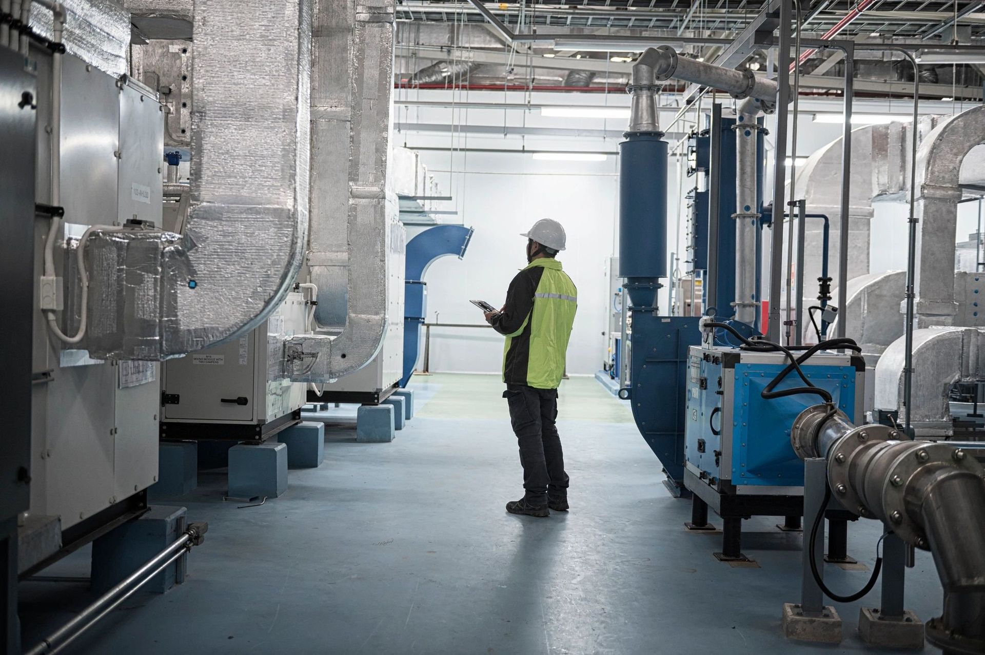 Worker in high-visibility vest inspecting industrial machinery in a factory room