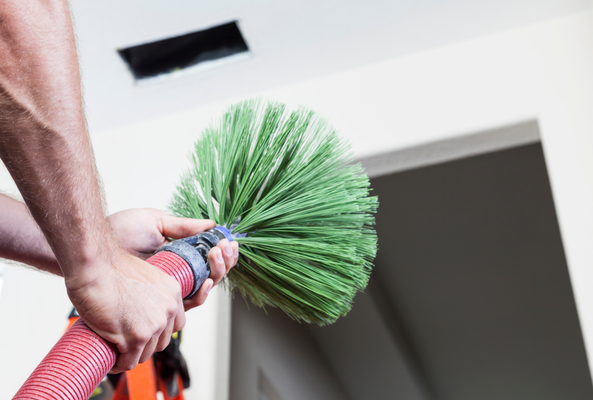 Hand holding a green feather duster near a ceiling vent indoors
