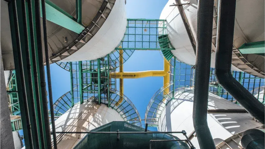 Upward view of industrial tanks and pipelines, representing manufacturing infrastructure and operations.