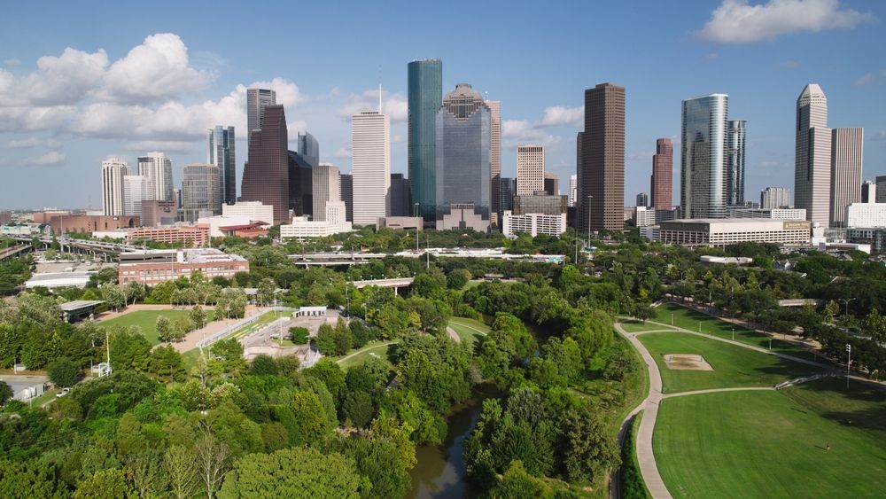 City skyline with modern skyscrapers beyond a green park and winding path under clear skies