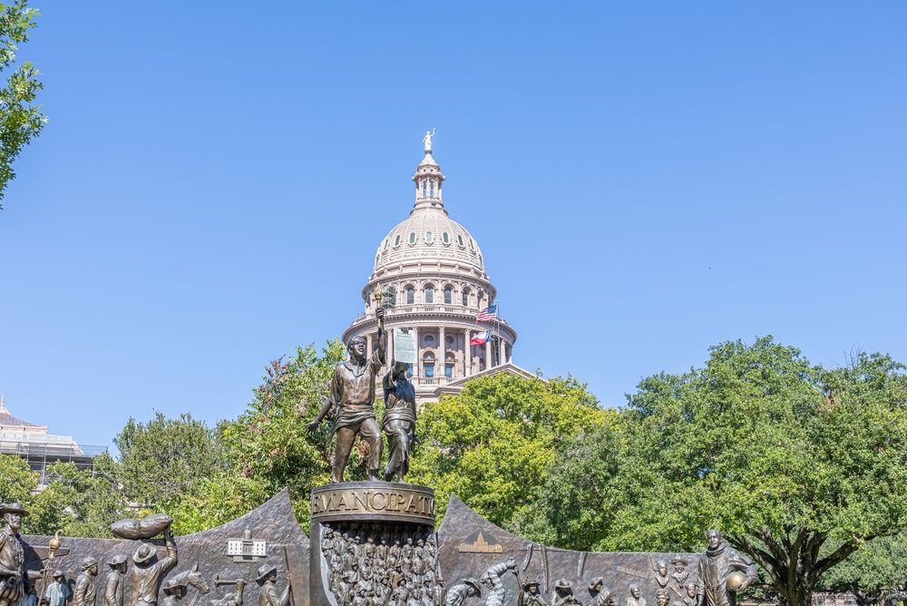 Dome of a historic building above trees and a stone wall under a clear blue sky