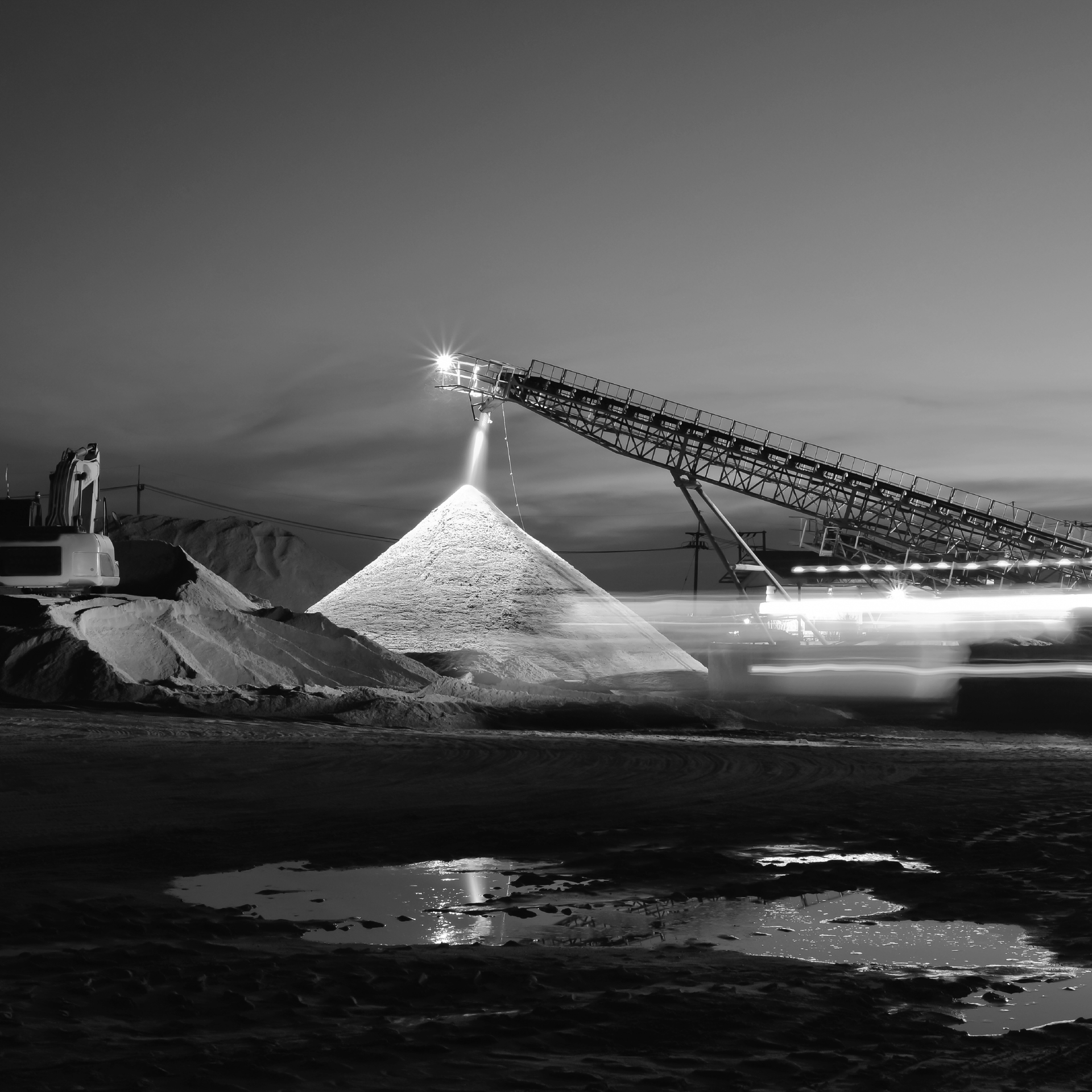 Black-and-white night mining scene with conveyor loading materials and heavy equipment in operation.