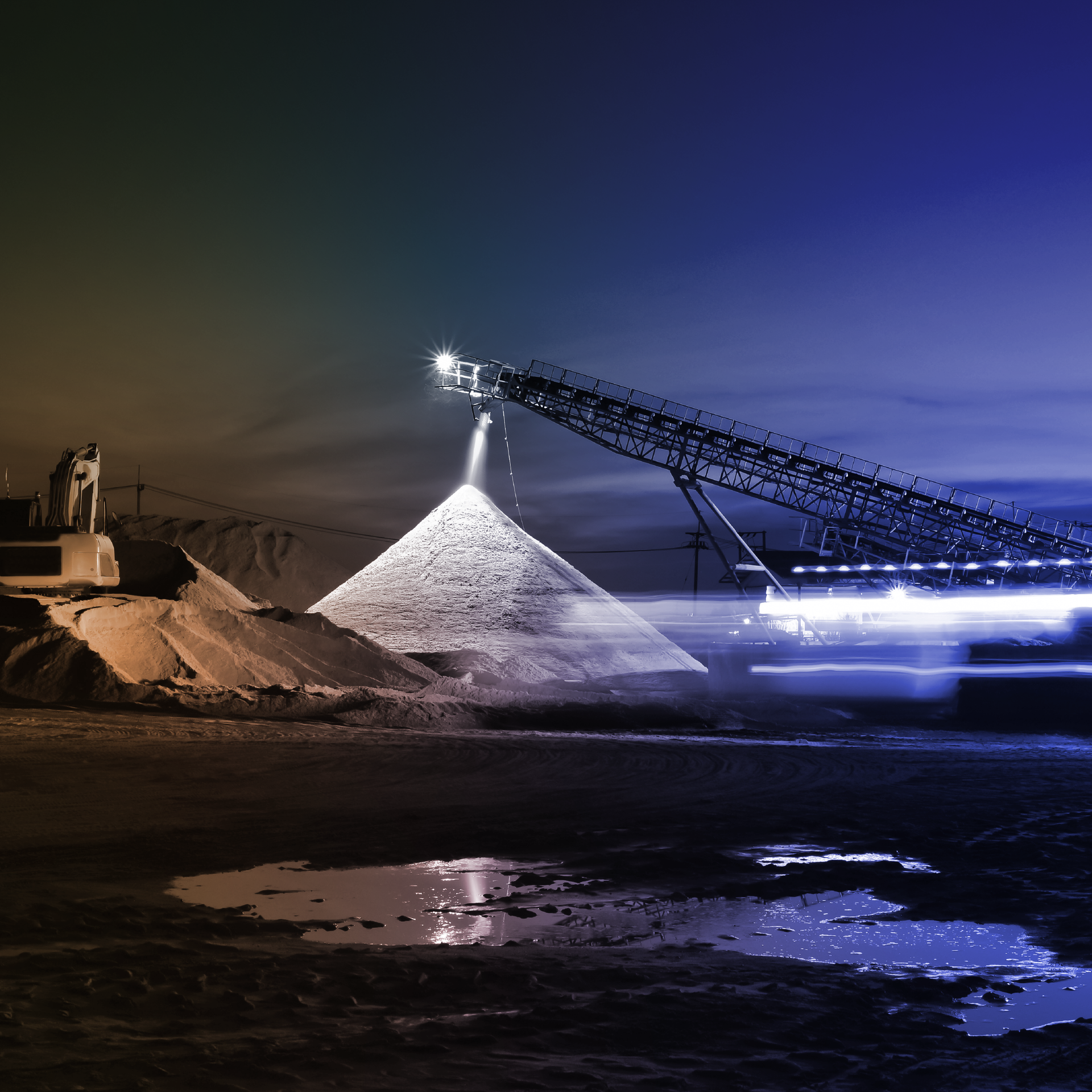 Nighttime mining site with conveyor piling materials, illuminated equipment, and industrial activity.