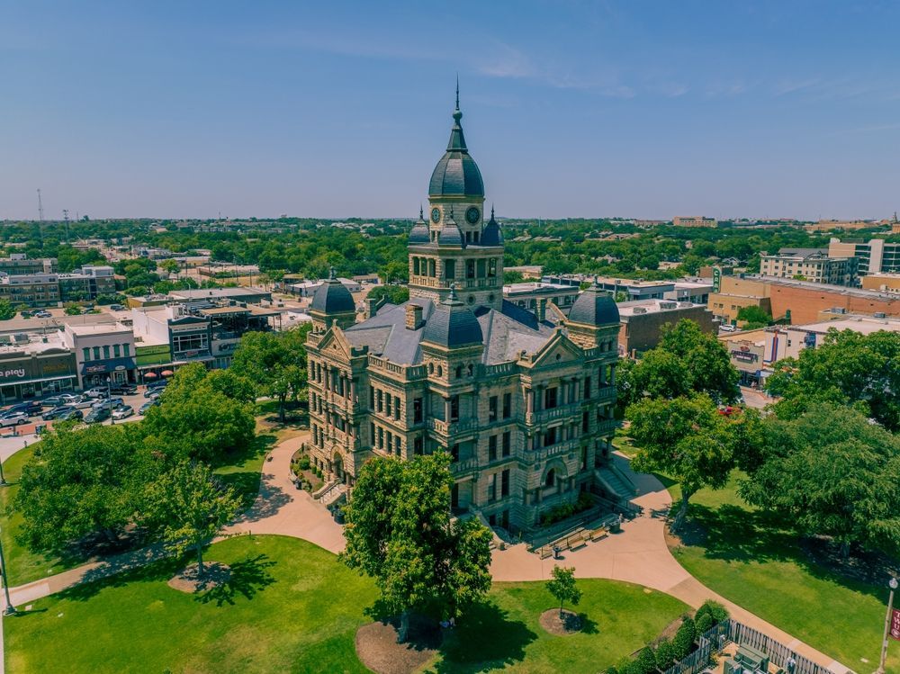 Historic stone capitol building with a central dome, surrounded by trees in a cityscape under a clear sky.