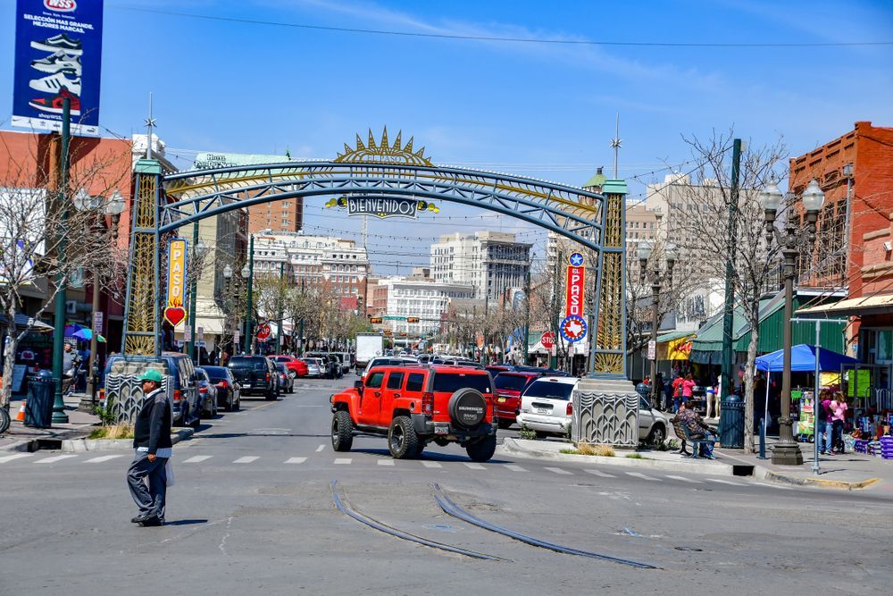 Busy city street with cars and pedestrians under a decorative archway on a clear day