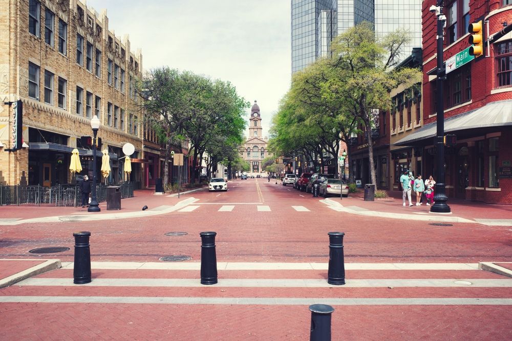Empty brick-lined city street with crosswalks, trees, and buildings on both sides