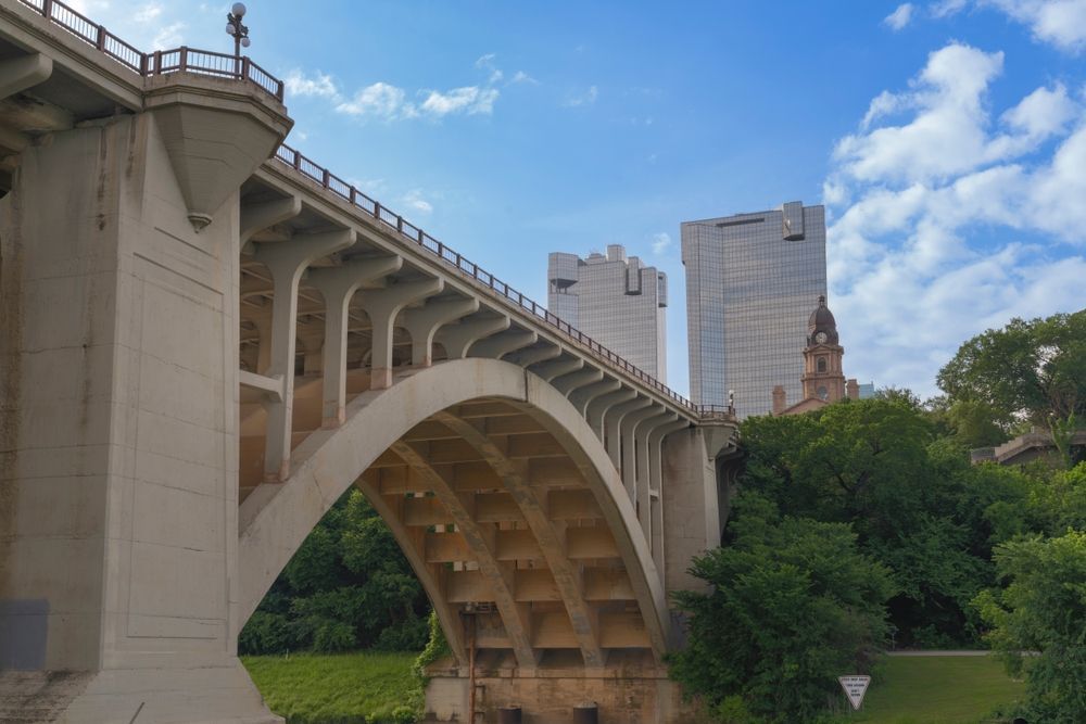 Stone arch bridge over a river with city buildings and blue sky in the background
