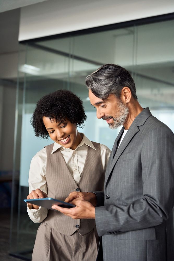 Two business professionals smiling while reviewing information on a tablet in a modern office setting.