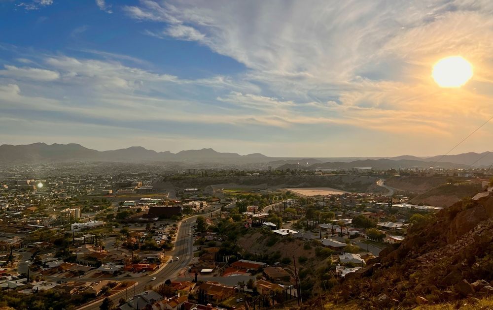 Sunset over a cityscape with mountains in the distance and a rocky hillside in the foreground