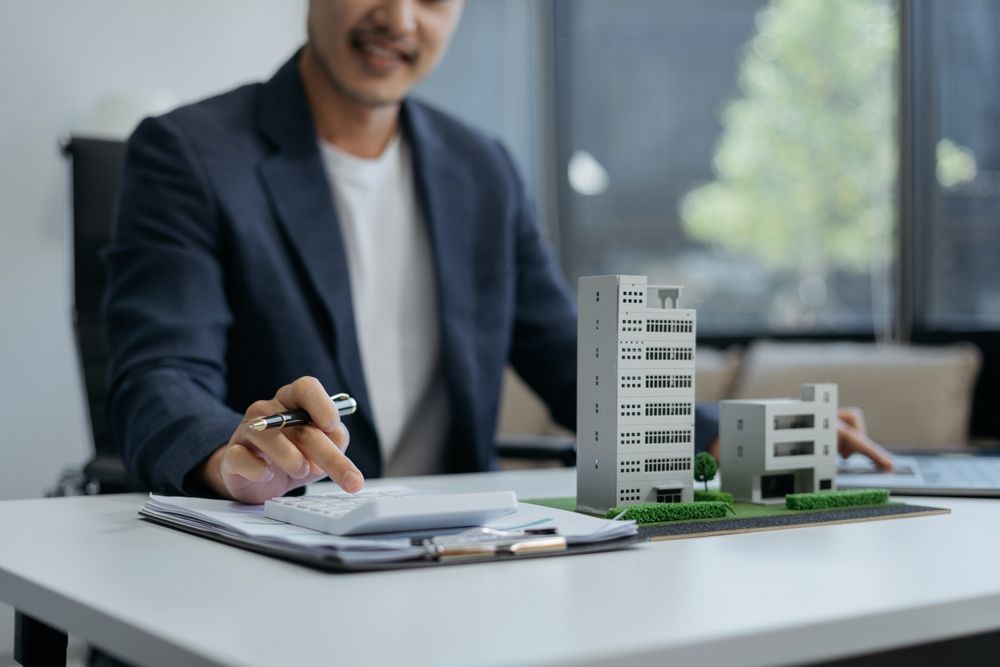 Real estate professional calculating property investment costs beside miniature building models.