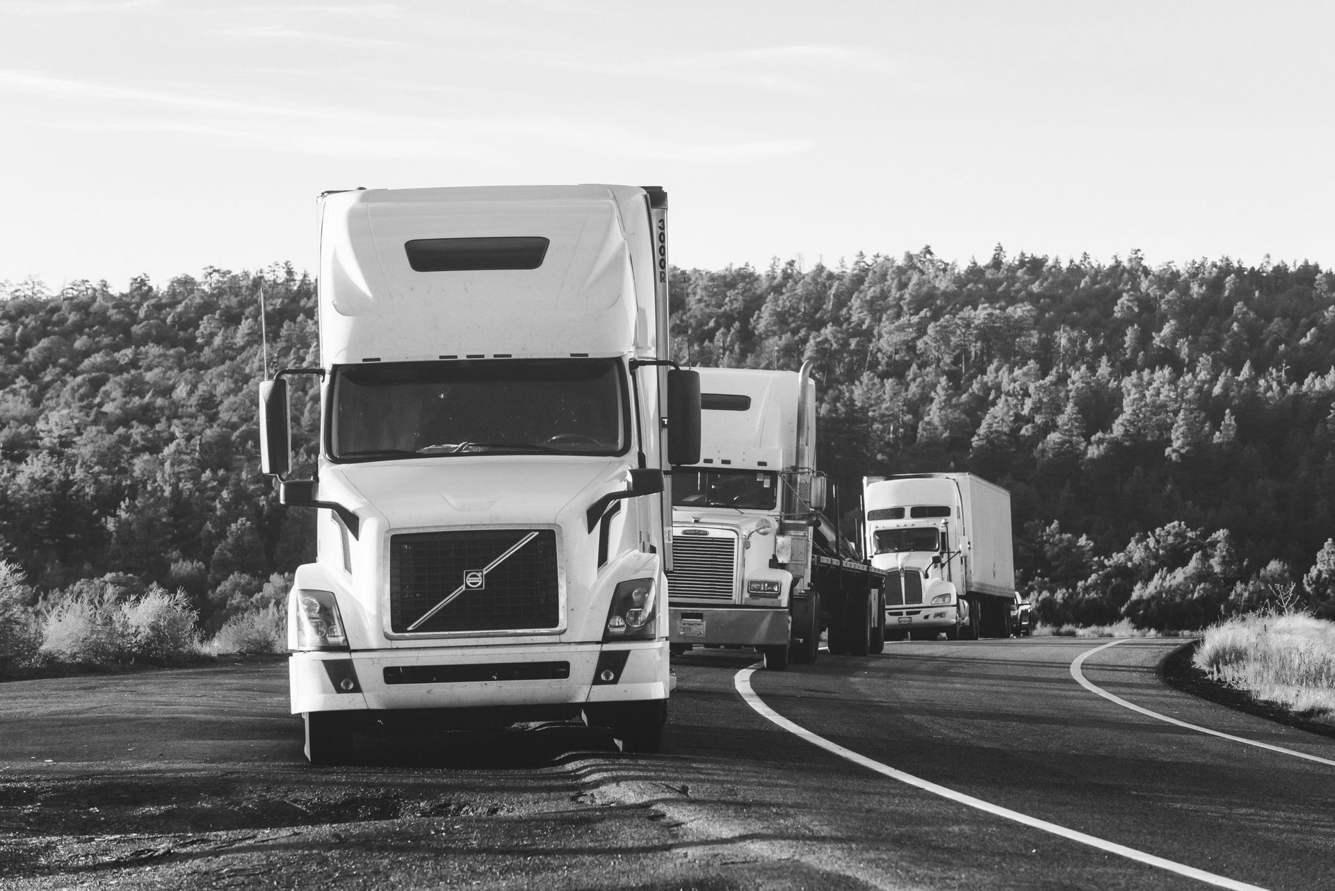 Line of semi-trucks driving on rural highway, representing commercial fleet operations and logistics.