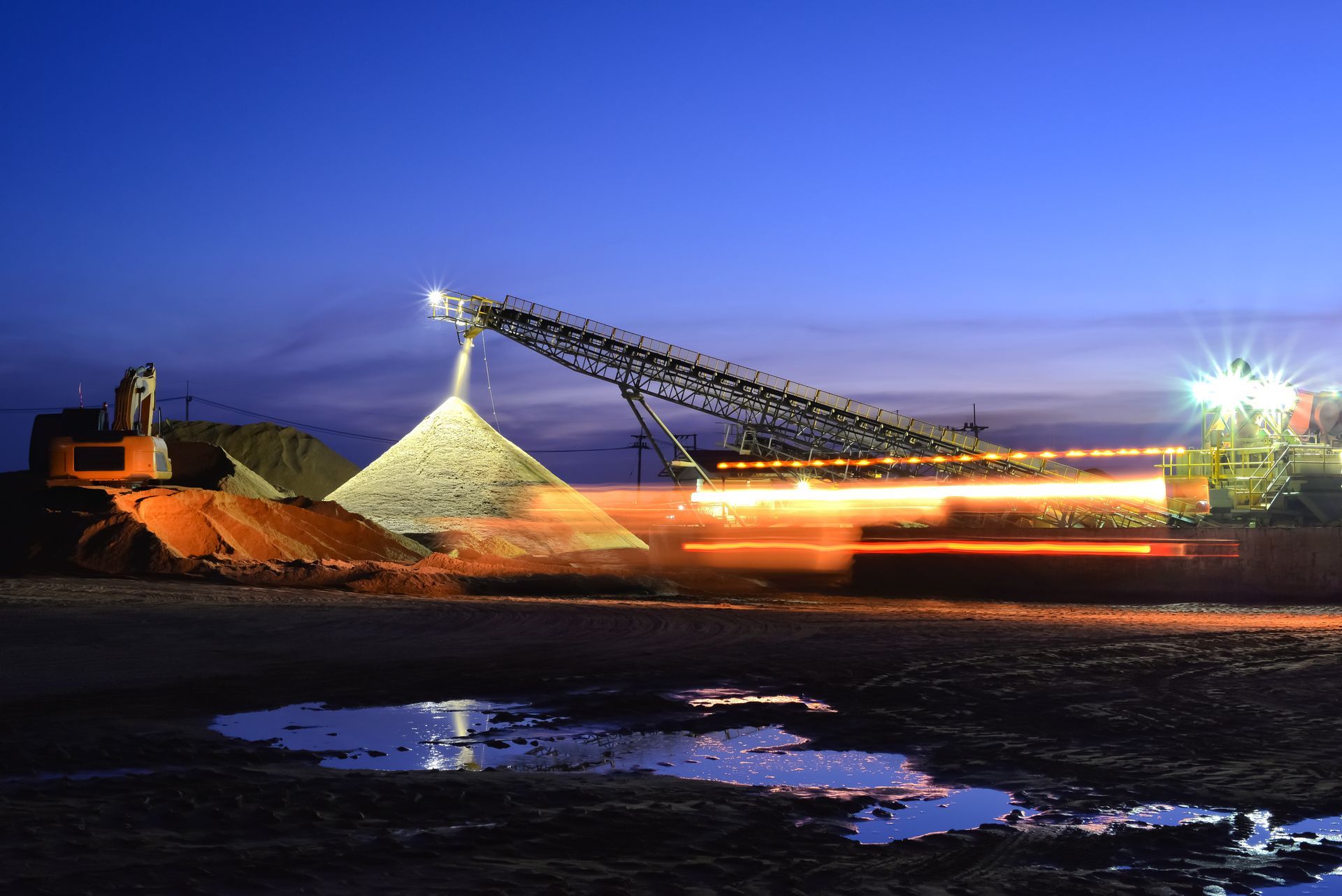 Mining site at dusk with conveyor loading materials, representing industrial operations and production.