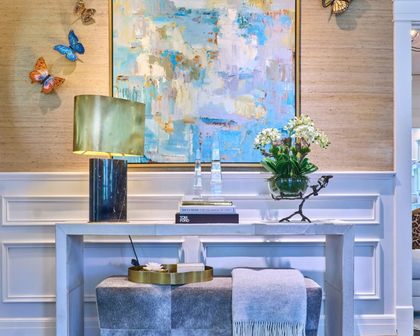 Elegant console table with lamp, flowers, abstract wall art, and blue butterfly decor in a bright room