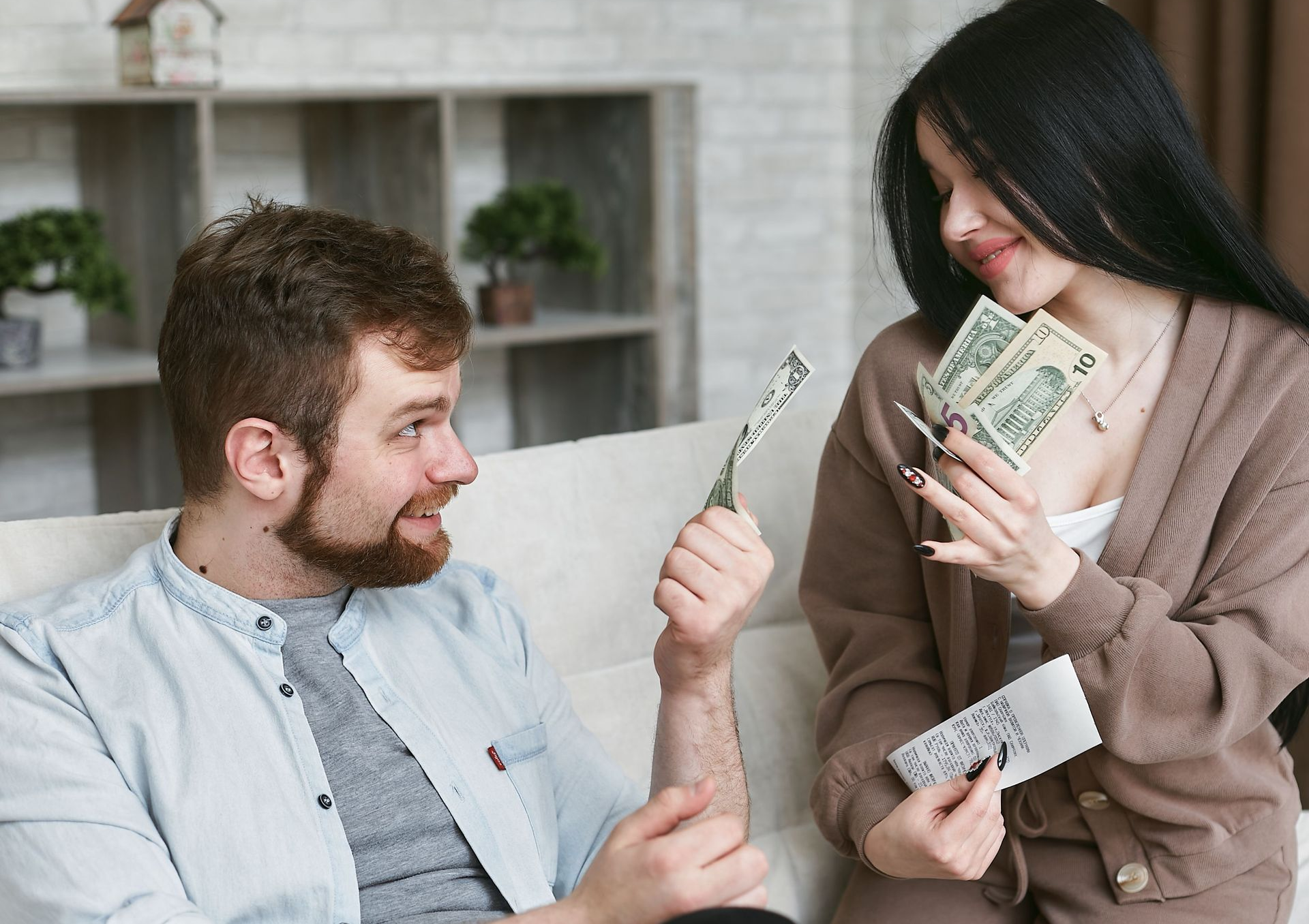 Two people in a room exchanging cash and a card, smiling on a sofa