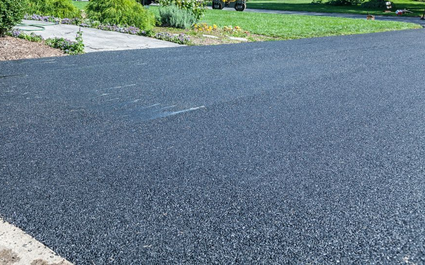 Freshly paved dark asphalt driveway beside a green landscaped yard and stone edging