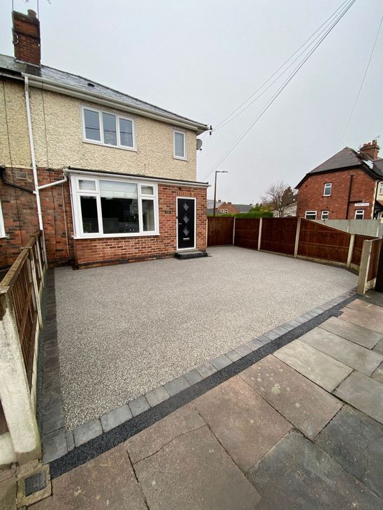 A modern, light-colored semi-detached house with a newly laid grey resin driveway and a dark border.