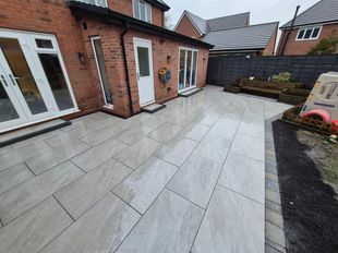 A modern two-story home with a white exterior, gray roof, and a large, newly paved gray resin driveway.