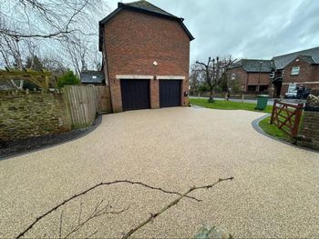 A view of a house with two dark garage doors and a light-colored, gravel-paved driveway, bordered by stone walls and lawns.