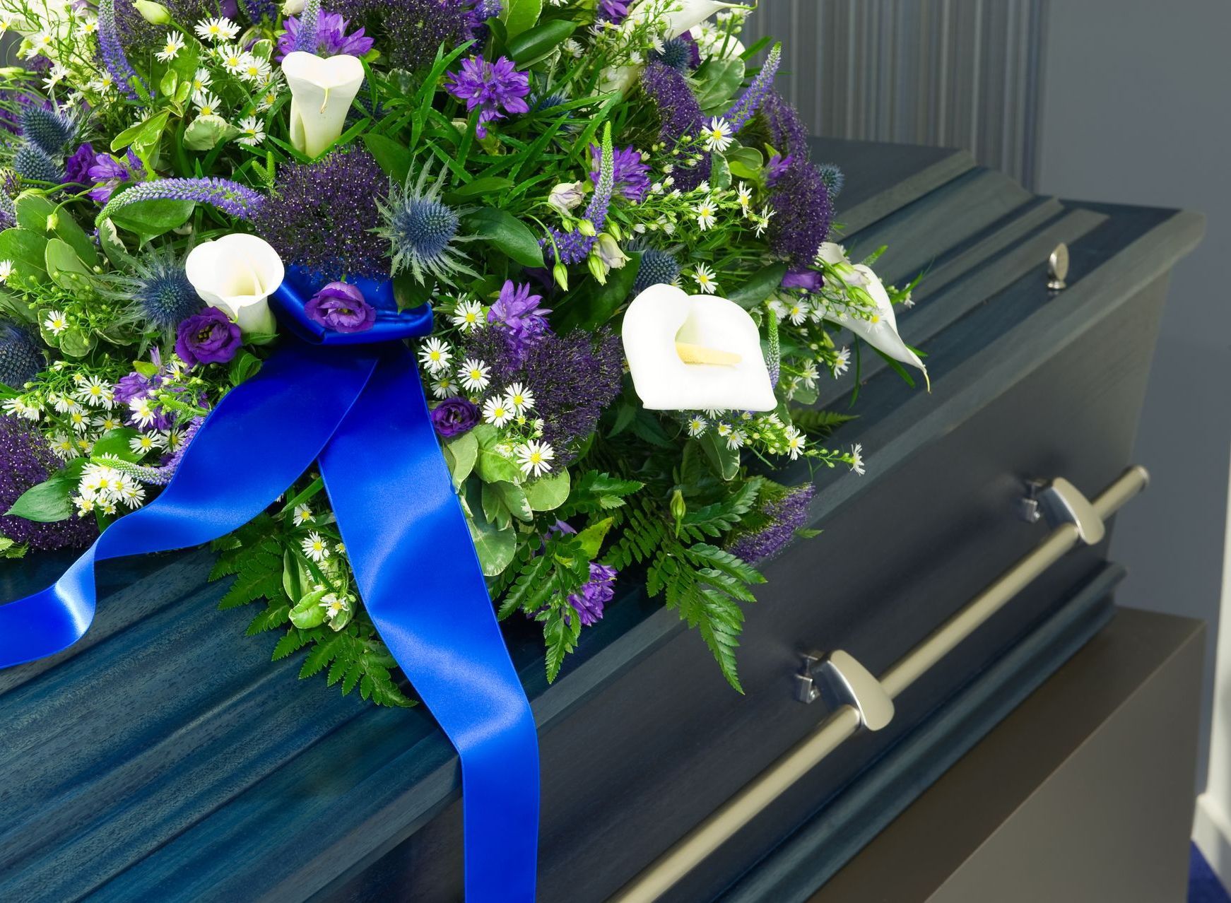 Purple and white funeral bouquet with blue ribbon resting on a dark casket handle