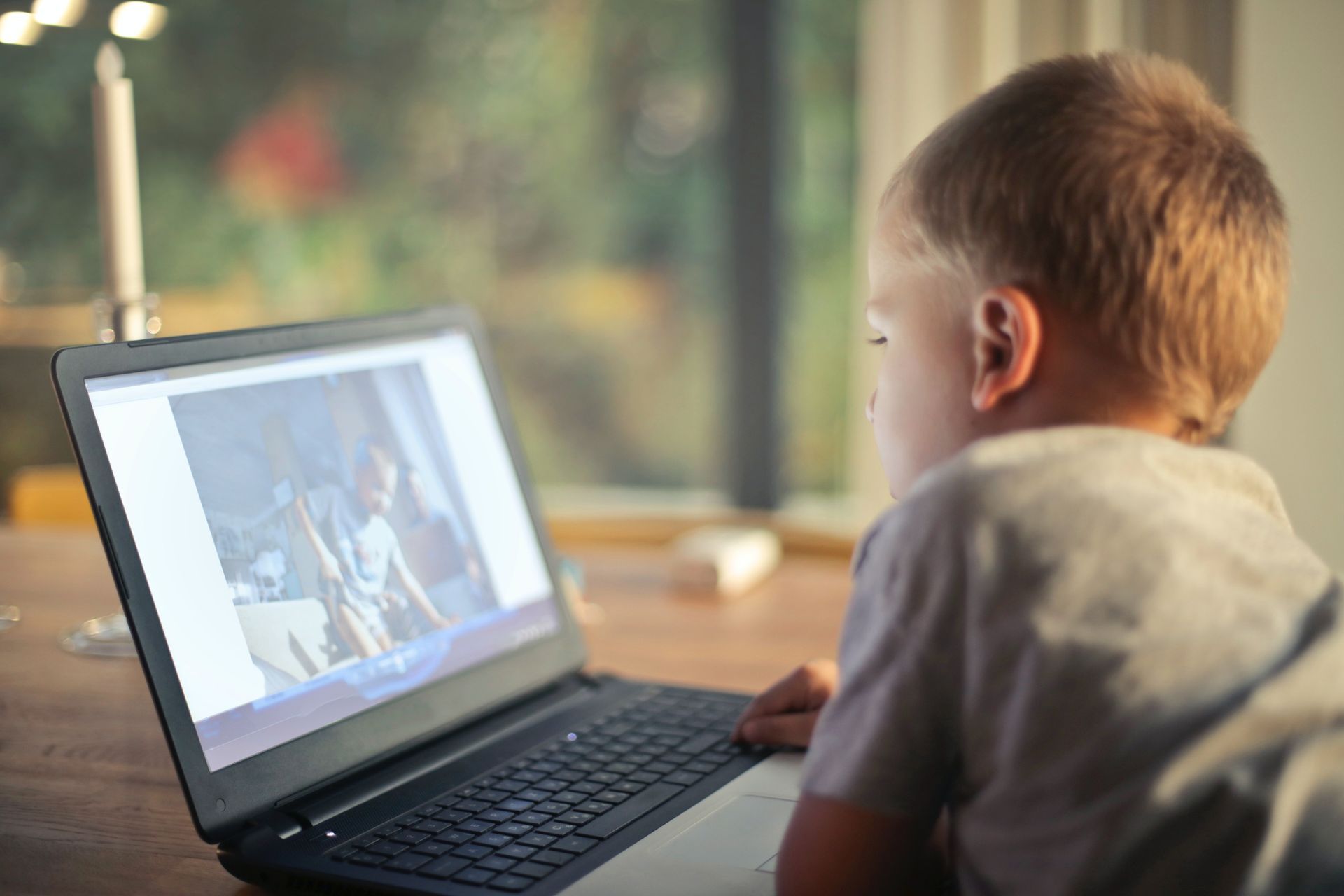 Child using a laptop at a table, watching a video in a bright room