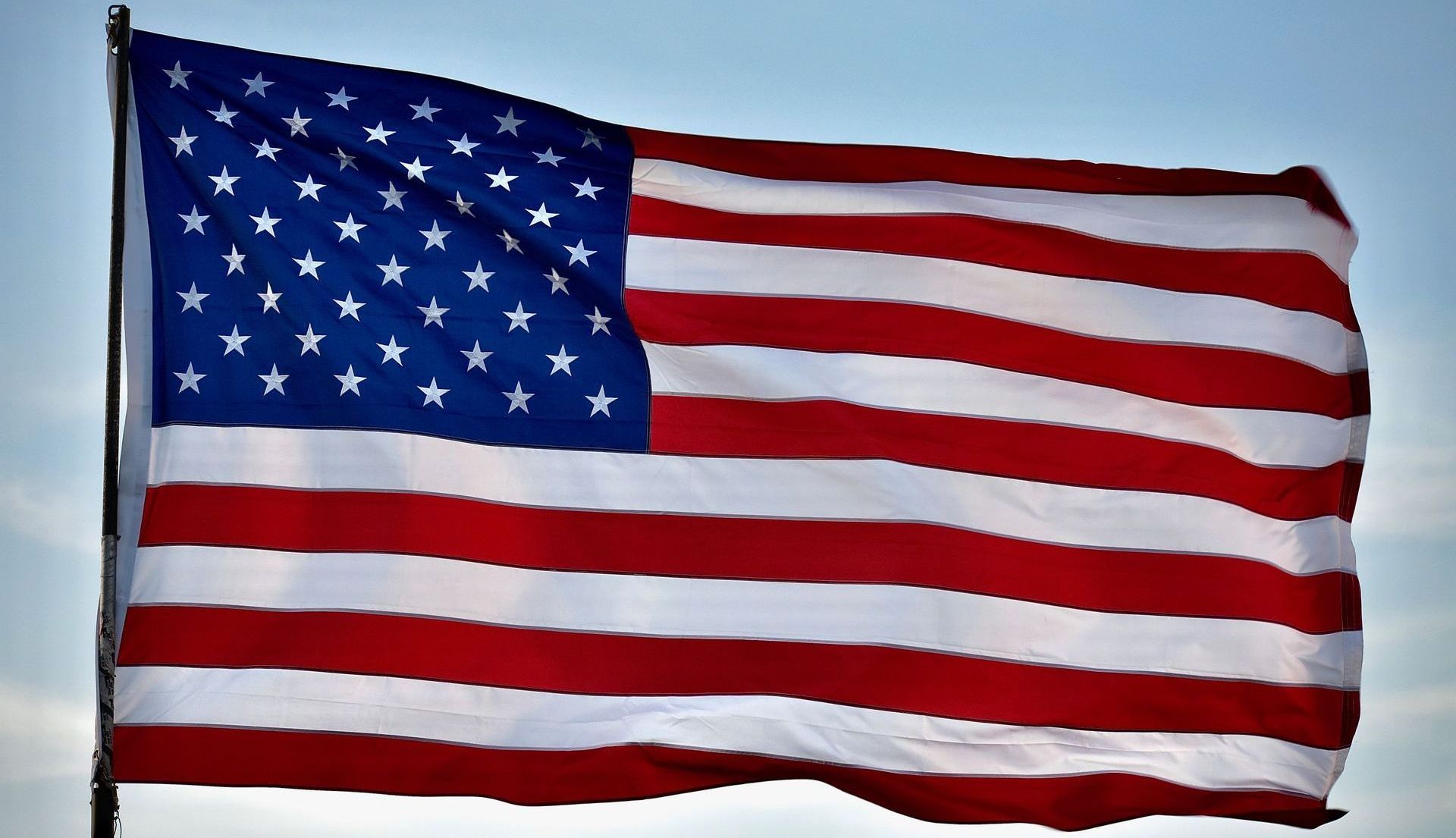 American flag waving in the wind with blue star field and red and white stripes.