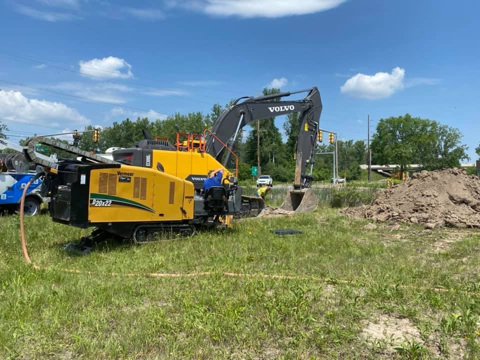 Yellow directional drilling machine in grassy field, blue sky.
