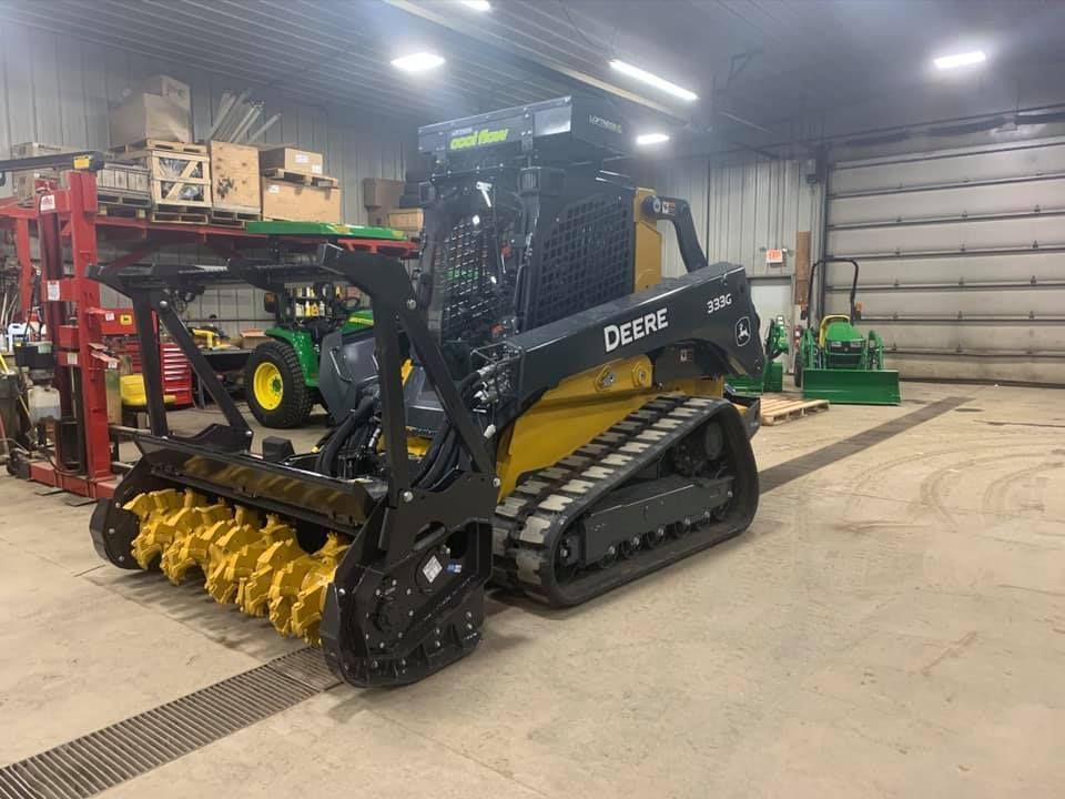 John Deere track skid steer with mulcher attachment in a warehouse.