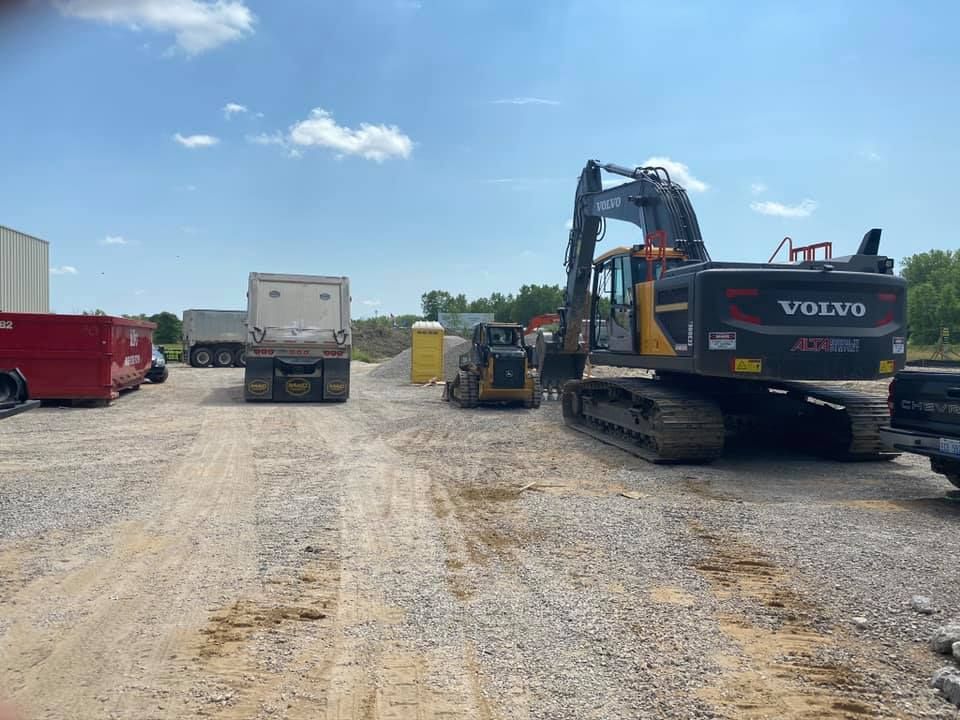 Construction site with an excavator, dump truck, and other equipment on gravel.