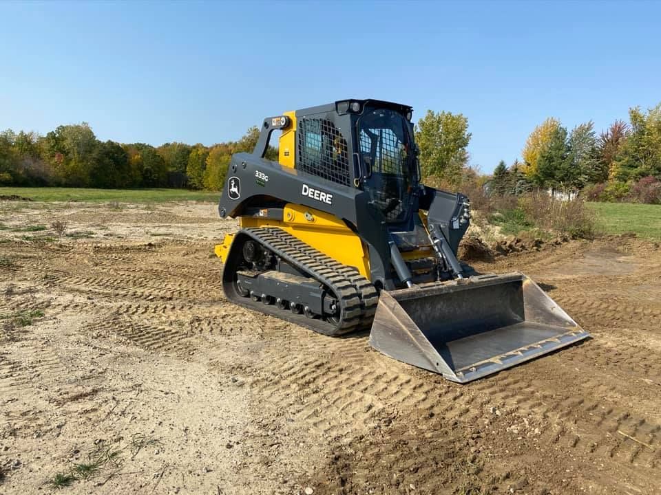Yellow and black track loader on dirt, with a bucket attachment, in an open field.