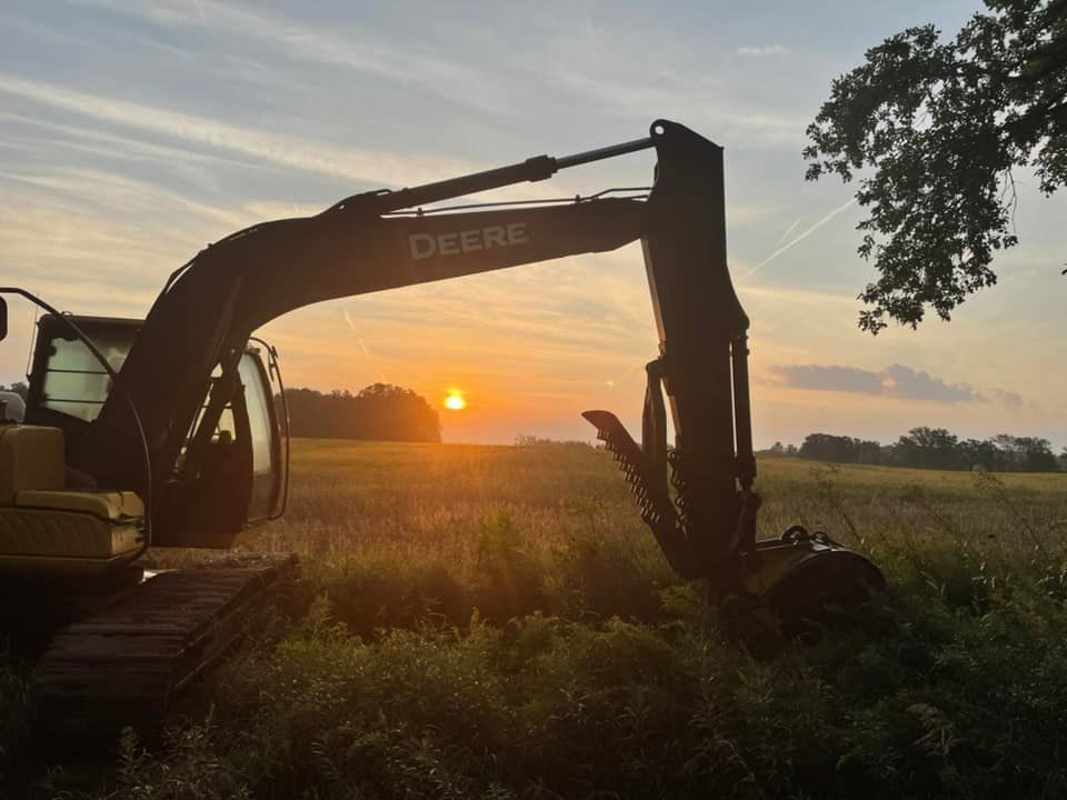 John Deere excavator silhouetted against a sunset in a field.
