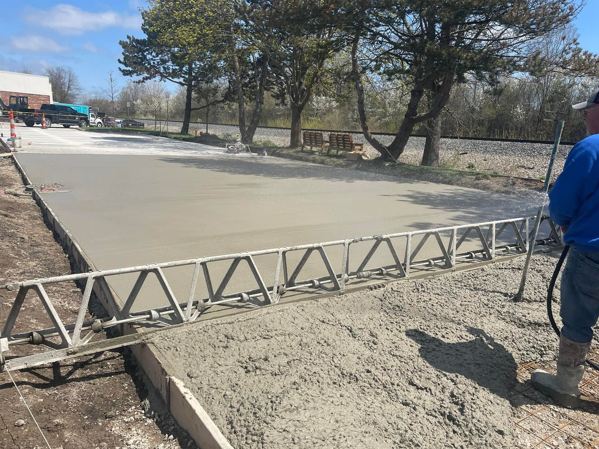 Concrete being leveled with a screed; a worker sprays water. Outdoors, on a sunny day.