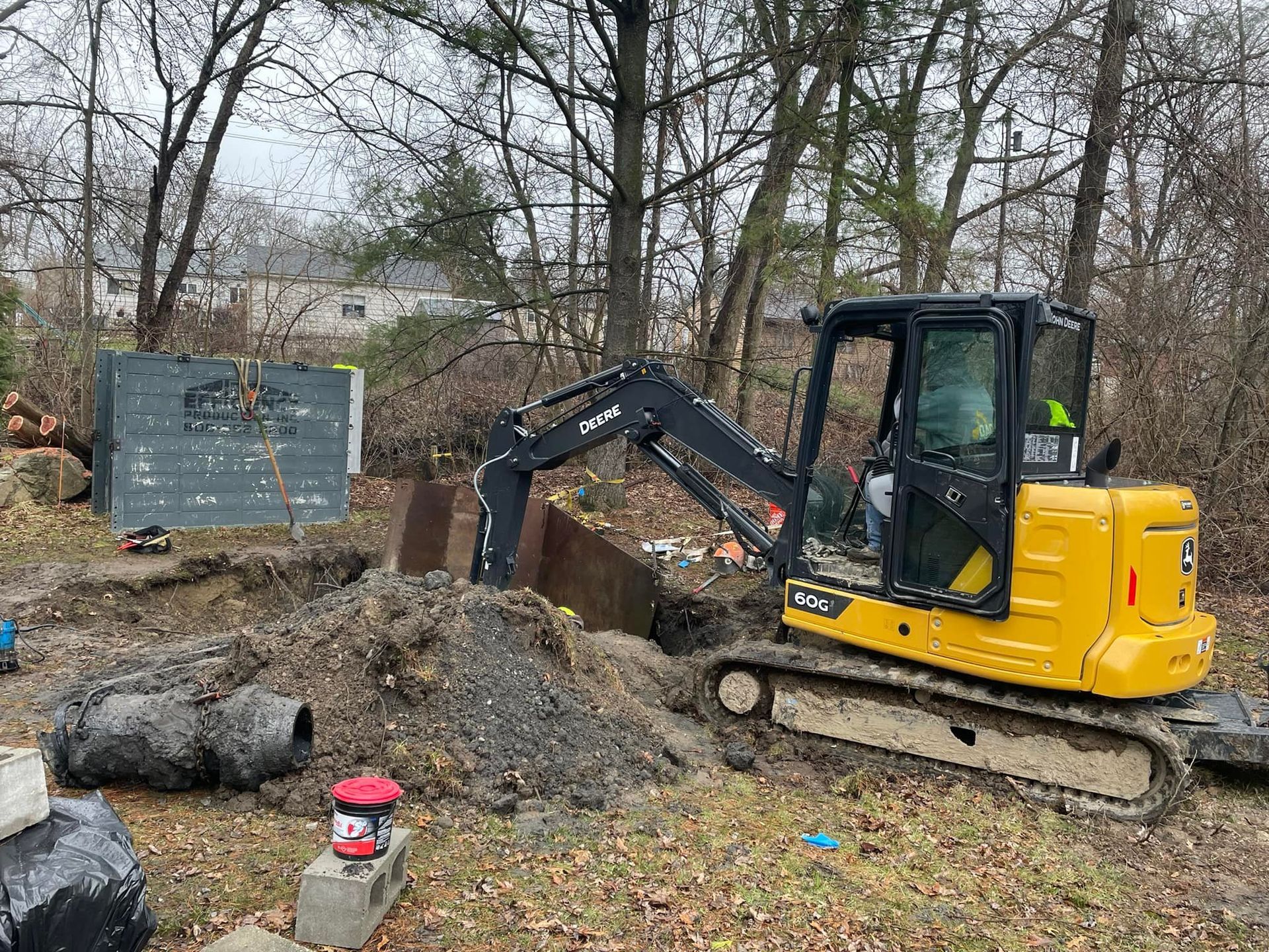 Yellow mini excavator digging in a yard near trees and a storage unit.