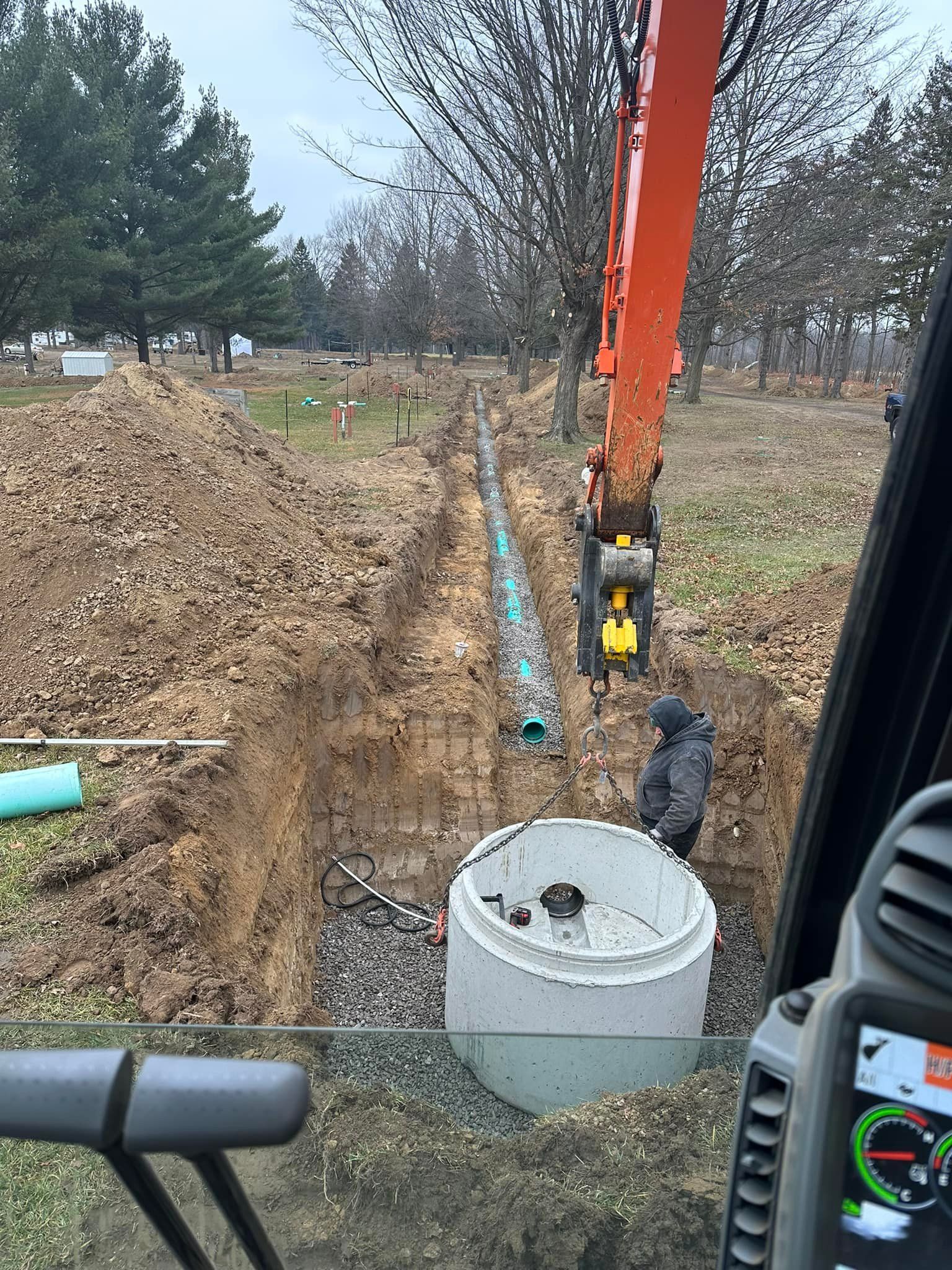 Construction site: Excavator and worker near an open trench, installing pipe and a large concrete tank.