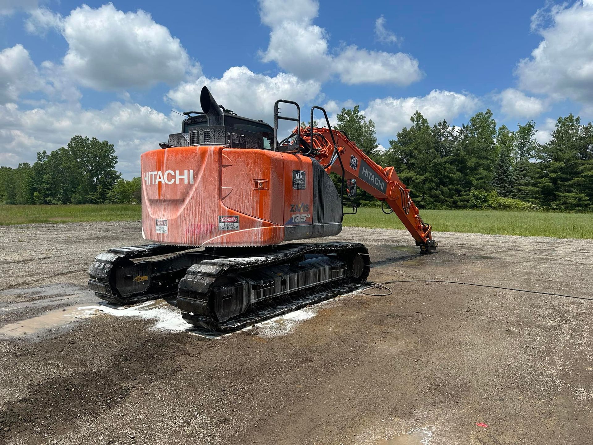Orange Hitachi excavator on gravel in a field under a blue sky.