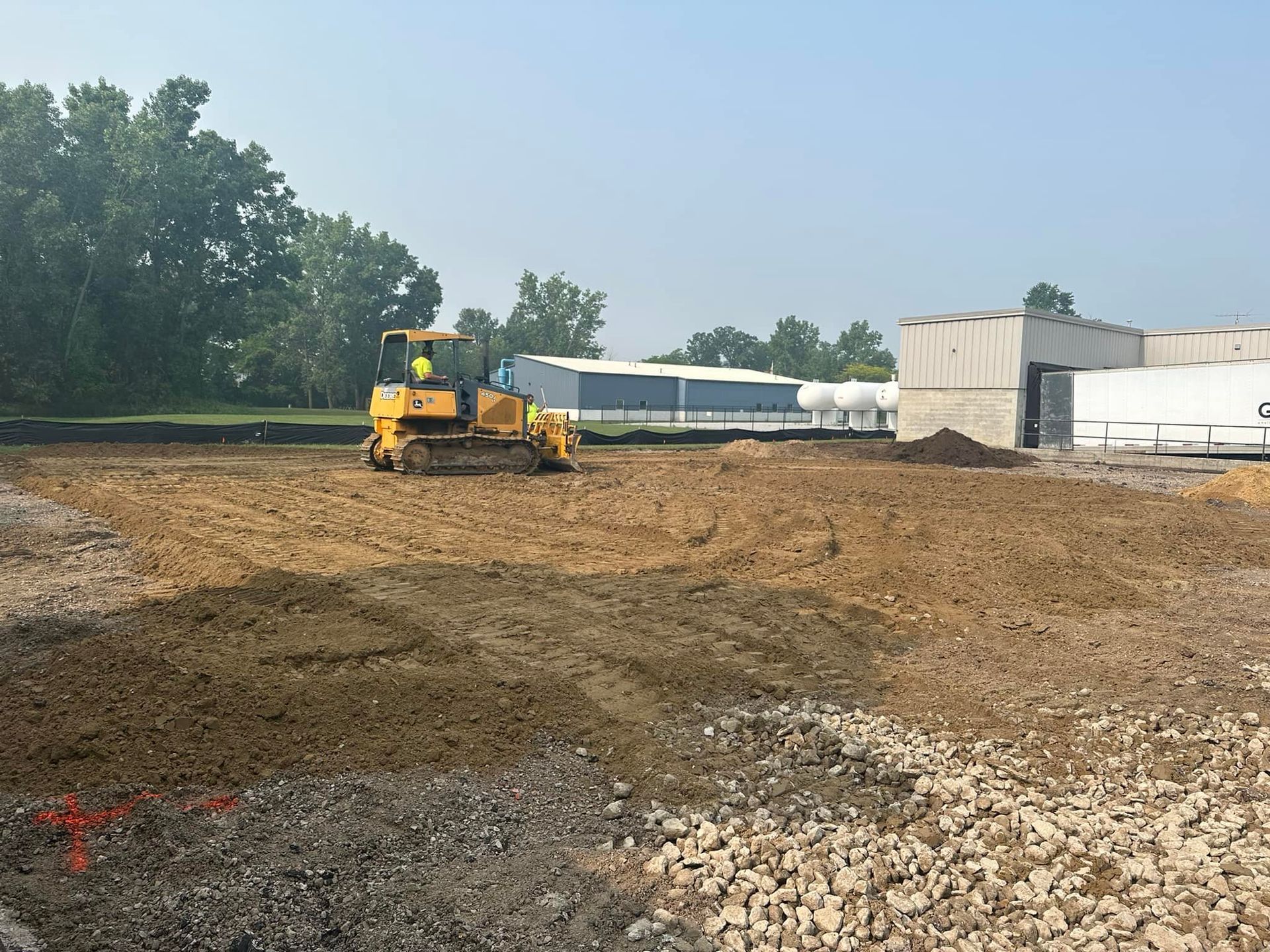 Yellow bulldozer leveling dirt at a construction site near a building under a blue sky.