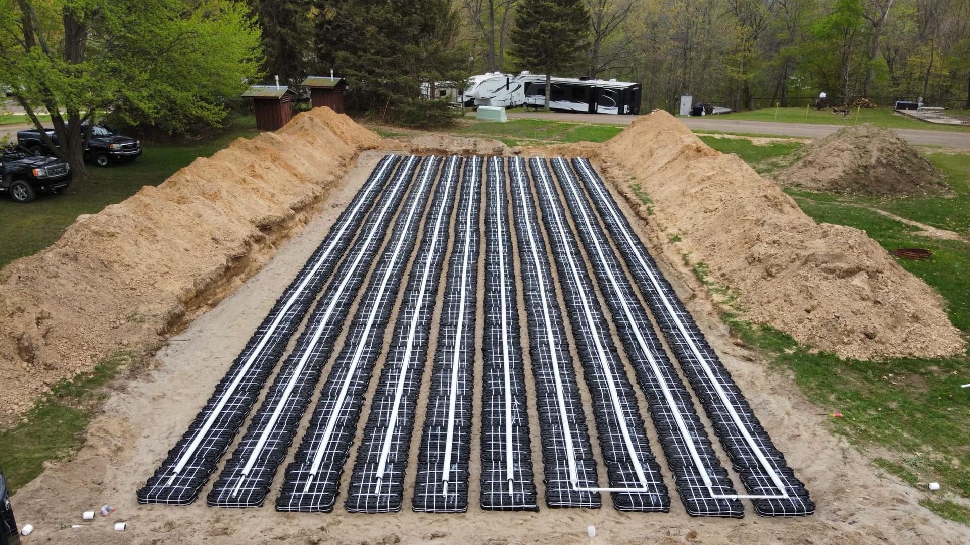 Large, excavated trench filled with parallel black pipes for a septic system.