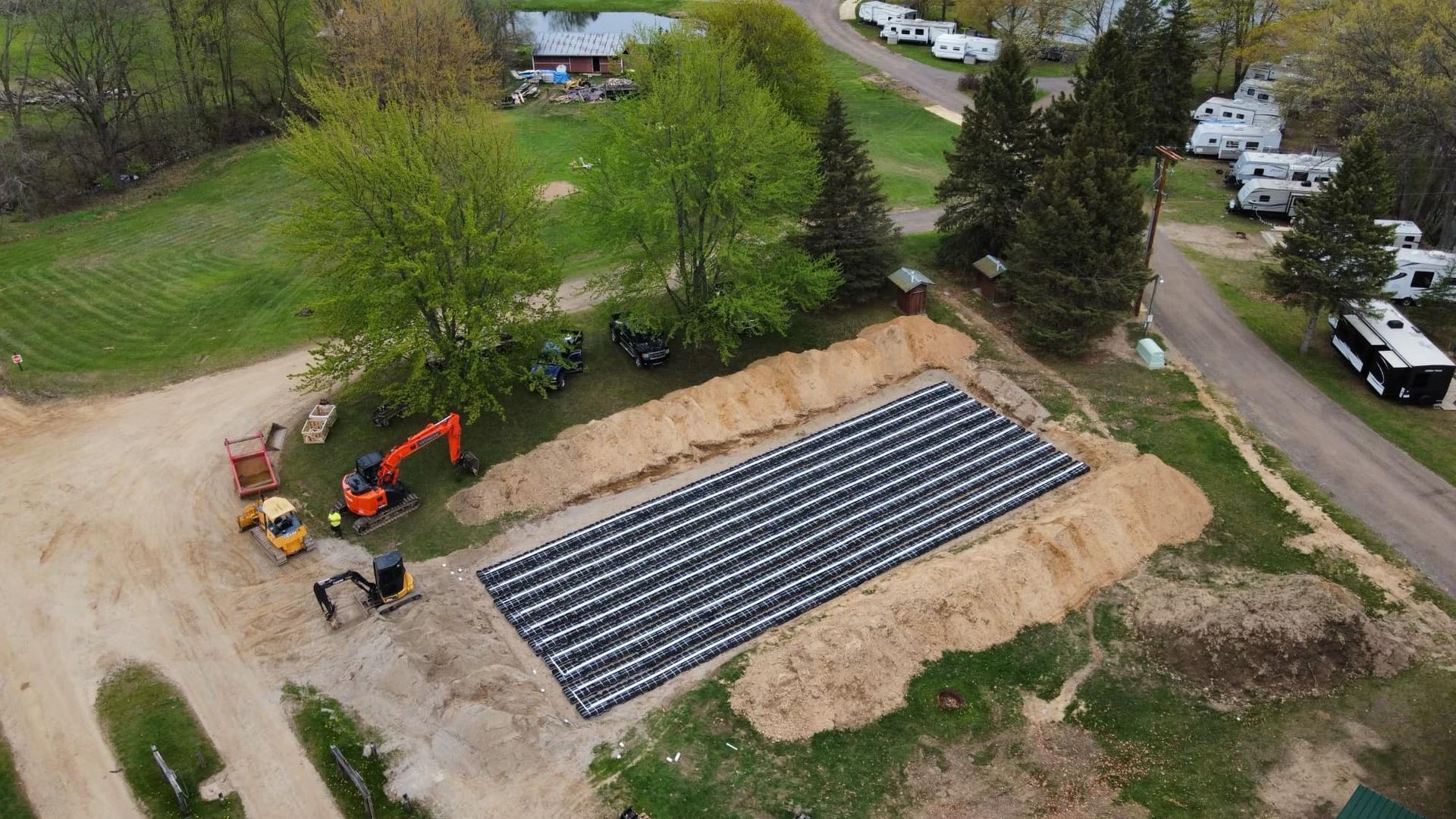 Aerial view: Construction site with heavy machinery, a large rectangular grid, and trailers.