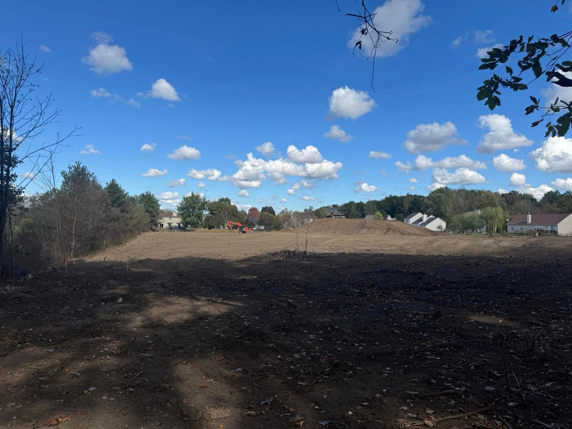 Cleared construction site with a blue sky and scattered clouds.