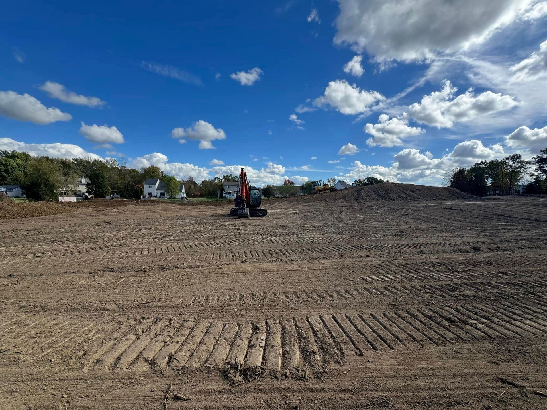 Construction site, backhoe on dirt, cloudy blue sky.