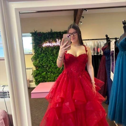 Woman in red formal dress taking a mirror selfie in a dress shop.