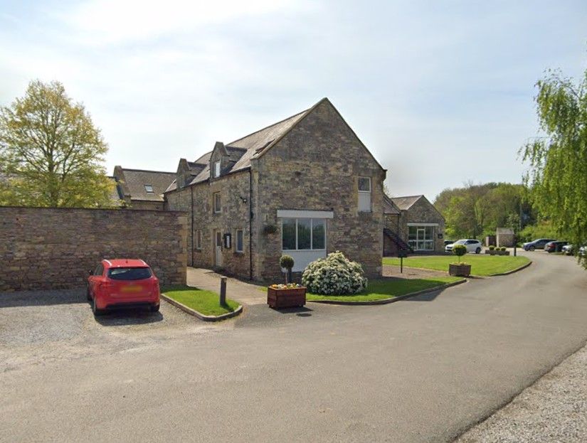 Stone building with red car parked in front, pathway and lawn.