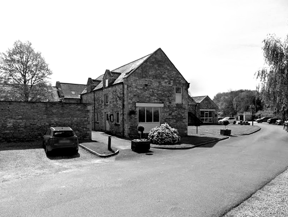 Stone building with driveway and parked cars; tree in the background.