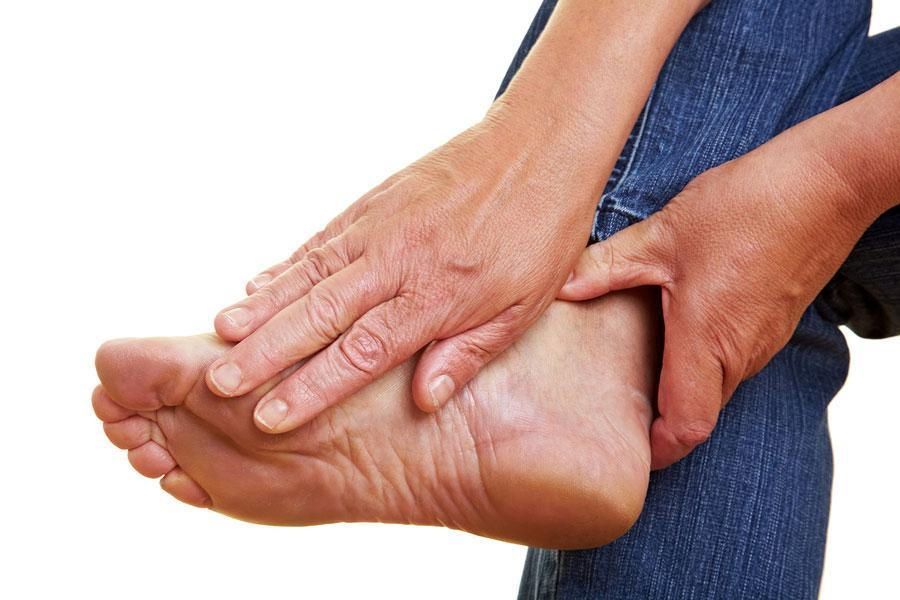 Person holding their foot, touching the heel and ankle, wearing blue jeans.