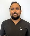 Man in black scrubs with a dark beard, looking at the camera. White background.